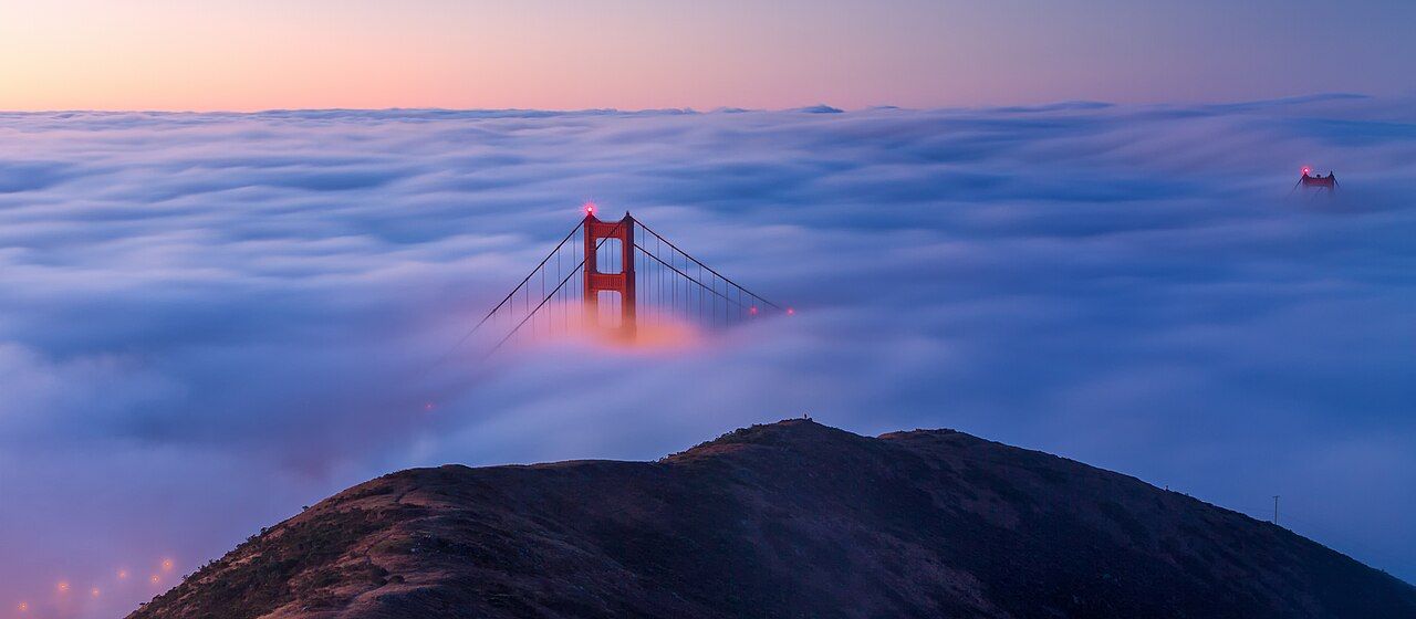 The Golden Gate Bridge as seen from the Marin Headlands at sunrise. Large parts of the bridge are covered by low, dense 