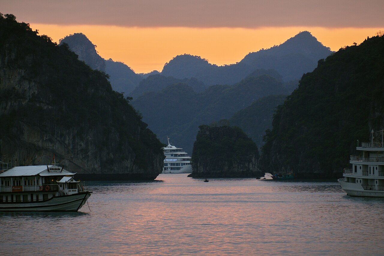 Cruise and tour boats anchored among karst limestone islands in Ha Long Bay at dusk.
